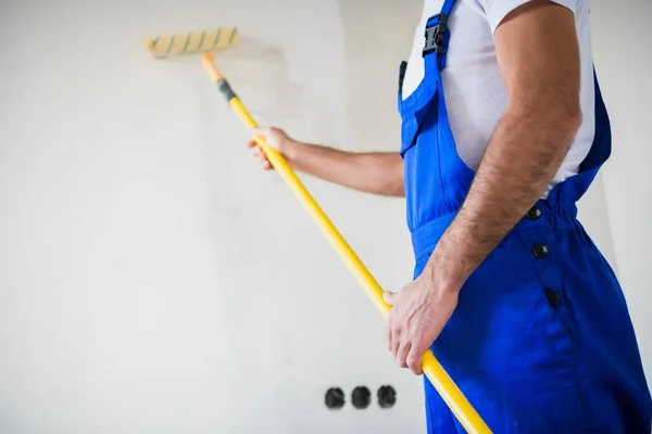 Chiudere, un uomo in tuta dipinge un muro in bianco con un rullo — Foto Stock