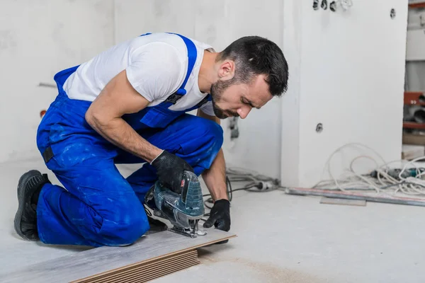 A carpenter in overalls cuts planks and lays laminate flooring — Stock Photo, Image