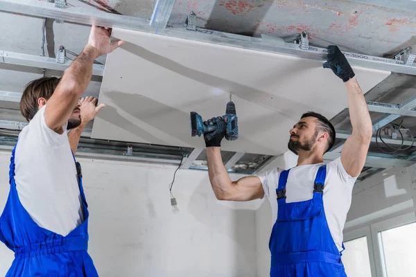 A builder and his colleague fix a plasterboard plate to the ceiling — Stock Photo, Image