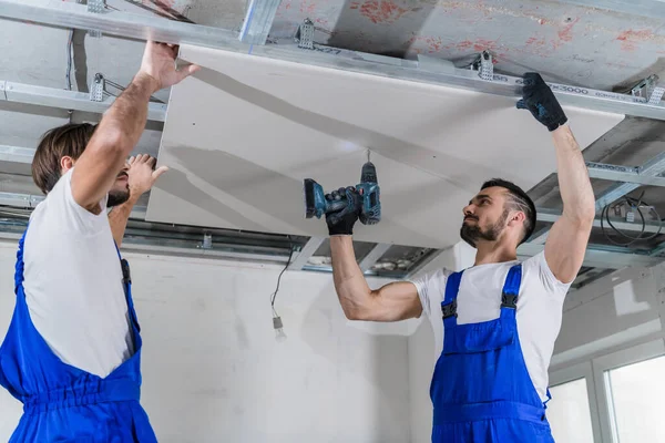 Ein Bauarbeiter und sein Kollege befestigen eine Gipsplatte an der Decke — Stockfoto