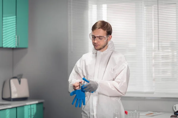 Assistente de laboratório veste luvas de borracha azul, preparando-se para fazer o seu trabalho. O conceito do perigo da propagação do vírus 2019-nCOV, COVID-19 — Fotografia de Stock