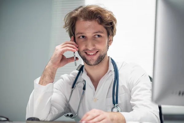 A smiling doctor talking on the phone, while looking at the computer screen — Stock Photo, Image
