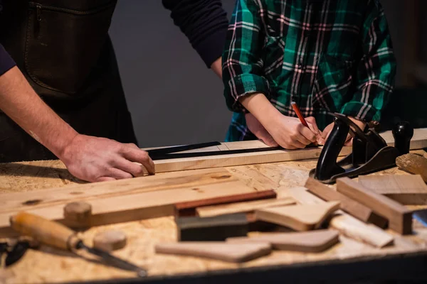 Primer plano del trabajo de un hombre y un niño en una mesa de carpinteros, en la mesa hay un plano, cincel, tablero, banco de trabajo, regla y otros artículos. — Foto de Stock