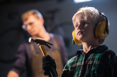 Marangoz dükkanındaki sevimli sarışın çocuk koruyucu gözlüklü ve kulaklıklı çekiçli, portresi olan..