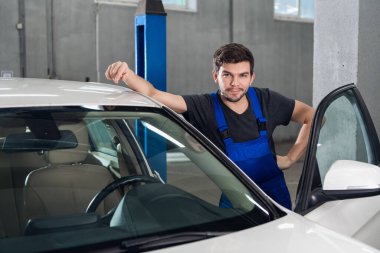 Üniformalı bir adam arabanın yanında duruyor.