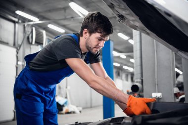 Tamirci arabanın kaputunun altındaki motoru kontrol ediyor.