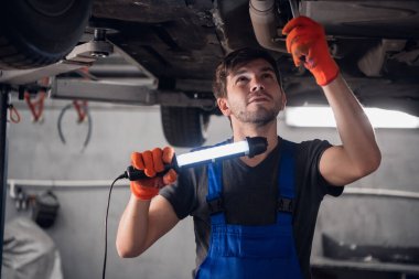 Teknisyen arabanın altını kontrol eder ve feneri yakar.