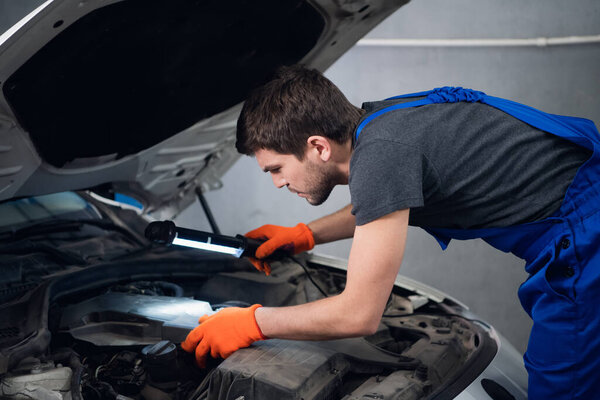 Repairer inspects a car engine using a flashlight