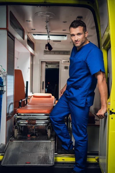 Retrato de un joven paramédico en uniforme parado en la parte trasera de un coche de ambulancia —  Fotos de Stock