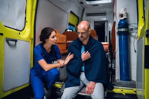 Enfermera hablando amistosamente con un hombre herido en una manta en un coche ambulancia — Foto de Stock