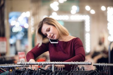 Perakende mağazasından alışveriş yaparken cep telefonuyla konuşan gülümseyen genç bir kadın.