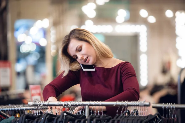 Улыбающаяся молодая женщина разговаривает по мобильному телефону, совершая покупки в розничном магазине — стоковое фото