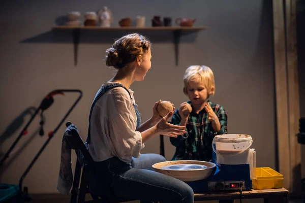 a young female Potter teaches a small boy to make a pot of clay.