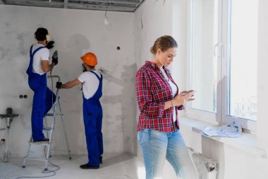 Cep telefonu kullanan kadın müşteri, arka planda çalışan tamirciler