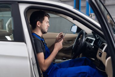 Atölye çalışanı arabada oturuyor ve akıllı telefon kullanıyor.