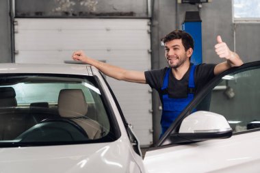 Bir tamirci arabanın yanında duruyor ve baş parmağını gösteriyor.