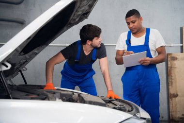 Tamirci, genç bir işçinin araba tamir etmesine yardım eder.