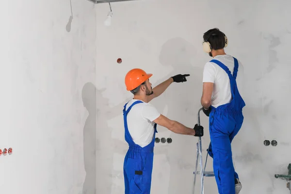 Ein Handwerker in Overalls steht auf einer Leiter, sein Kollege hilft ihm — Stockfoto