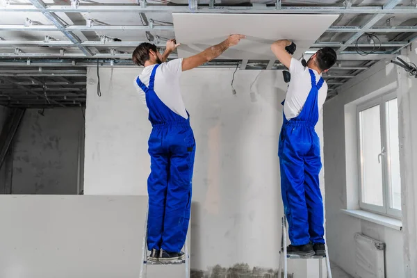 Mavi tulumlu tamirciler apartman dairesinde tavan yapıyor.