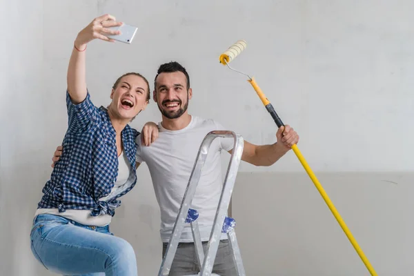 Man and woman taking selfie on the background of the wall with a stepladder and roller — Stock Photo, Image