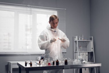 Koruyucu giysiler içindeki genç bilim adamı laboratuvar odasında bir kağıt parçasını yakıyor.