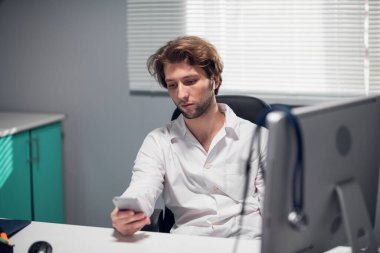 Telsiz kulaklıklı yorgun doktor telefondaki sesli mesajlarını kontrol ediyor.