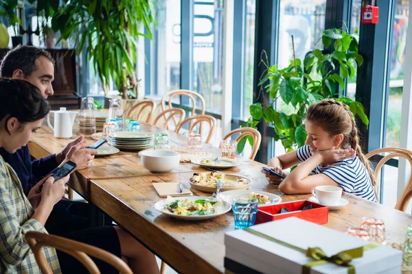 Een gezin van drie in het café, iedereen aan de telefoon. — Stockfoto