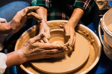 Çömlekçi çarkında kil tabaklarını modelleme süreci, genç bir kız ve bir çocuğun elleri..