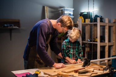 Deneyimli bir marangoz atölyede oğluna çeşitli aletlerin çalışmalarını gösterir..