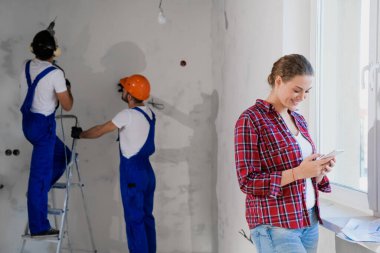 Cep telefonu kullanan bir kadın, arka planda çalışan üniformalı bir adam.