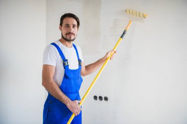Gülümseyen işçi duvarın yanında duruyor ve elinde bir silindir tutuyor.