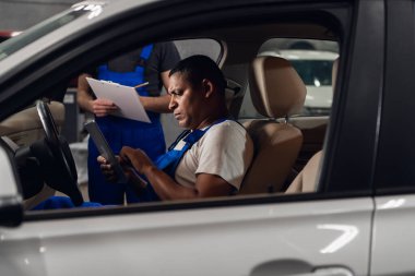 Araba servisi çalışanı arabada oturuyor ve tablet kullanıyor.