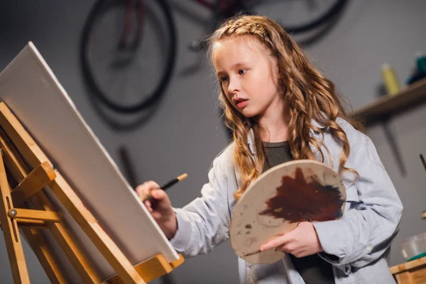 Una pequeña artista dibuja un cuadro con un pincel en el estudio. Una joven colegiala con talento — Foto de Stock