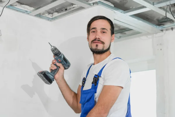 Trabajador con un taladro y un mono mirando a la cámara — Foto de Stock