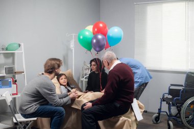 Kazadan sonra güzel, küçük bir kızı ziyarete gelen bir aile. Kız hastanede yatıyor. Tekerlekli sandalyesi köşede.