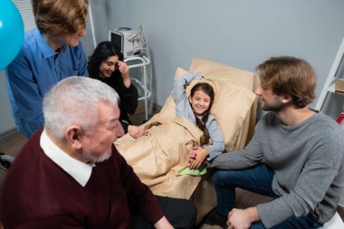 Neşeli bir aile hastane koğuşundaki küçük bir kızı ziyaret ediyor.