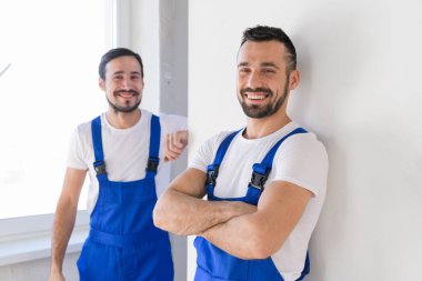 Tulumlu iki inşaat işçisi kameraya bakıyor.
