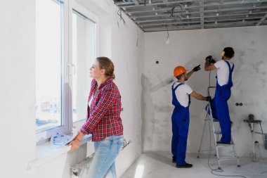 Bir müşteri pencerenin yanında duruyor ve belgeleri inceliyor, arka plandaki genel işçiler çalışıyor