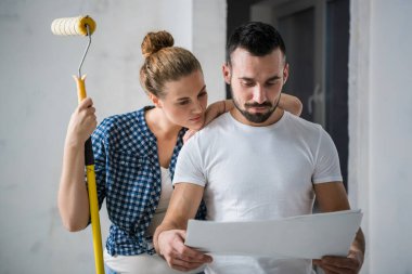 Çiftlerin ev planları ellerinde ve gülümsüyorlar.