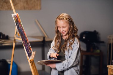 Bir sanat okulu öğrencisi bir atölyede tuval çizimi için paletin renklerini karıştırıyor..
