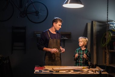 Genç bir baba ve küçük oğlu marangozların atölyesinde ağaçtan oyuncak yapıyorlar..