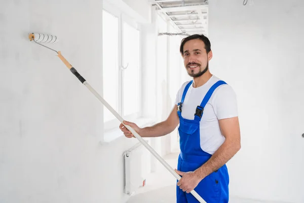 Trabalhador geral bonito em macacão pinta a parede com um rolo — Fotografia de Stock