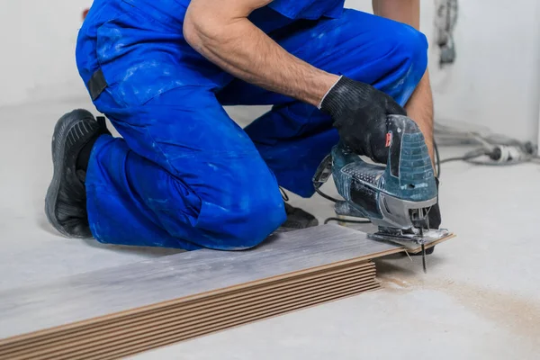 Um homem de macacão corta pranchas e coloca piso laminado — Fotografia de Stock