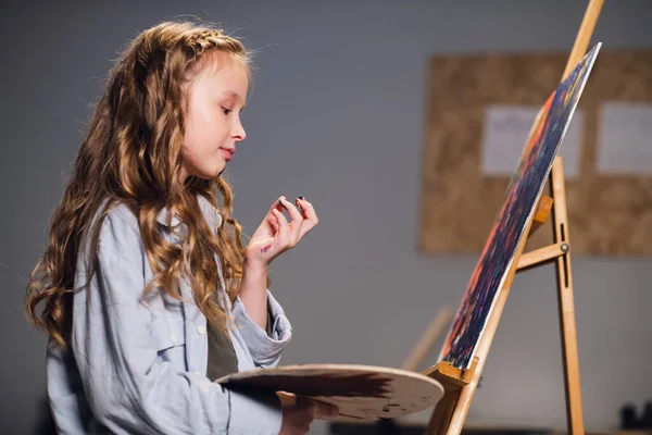 Una estudiante de arte mezcla colores en una paleta para dibujar su lienzo en un taller. —  Fotos de Stock