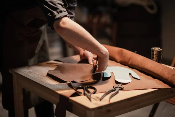 Un joven se dedica a la artesanía familiar de hacer zapatos de cuero en un taller. — Foto de Stock
