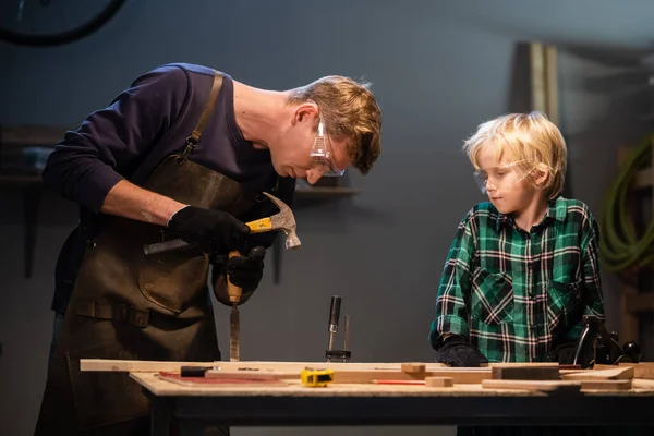 Un carpintero experimentado muestra el trabajo de varias herramientas a su hijo en el taller. — Foto de Stock