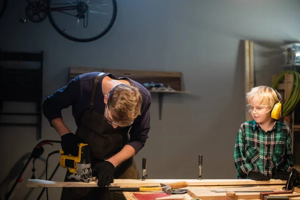 Un carpintero joven está enseñando carpintería a un niño en su taller. — Foto de Stock