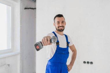Neşeli adam kameraya matkapla işaret ediyor.