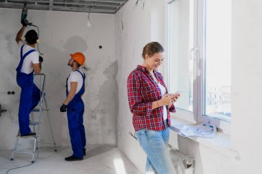 İşçiler matkap ve merdiven kullanıyor, telefonda yazan kadın.