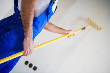 Yakından, tulumlu bir işçi duvarları beyaza boyardı.